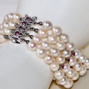 Peut inclure: Un bracelet en perles blanches avec un fermoir argenté orné de petites pierres rouges.