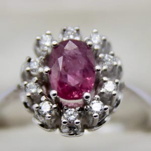Op de afbeelding: Een zilveren ring met een grote ovale roze robijn omringd door kleinere diamanten.