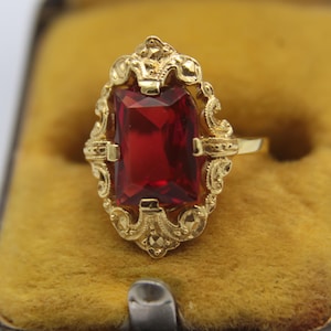 Peut inclure: Une bague en or avec une grande pierre précieuse rectangulaire rouge sertie dans un motif de filigrane.