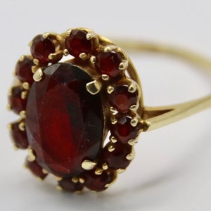 Può includere: Un anello d'oro con un grande granato rosso ovale circondato da granati rossi più piccoli.