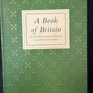Puede incluir: Un libro antiguo titulado "A Book of Britain" con una cubierta verde adornada con un patrón repetido de flores doradas y diseños de estrellas blancas. El título está en un marco rectangular blanco.