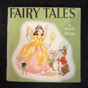 Può includere: Un libro vintage "Fairy Tales" con copertina verde. La copertina presenta una fata in abito giallo e corona, con una bacchetta, con un coniglio e due piccole figure. Il testo "A Pixie Book" è presente sulla copertina.