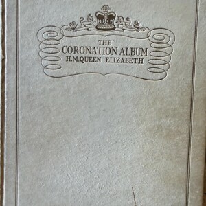 Op de afbeelding: Lichtbeige albumomslag met de titel "The Coronation Album H.M. Queen Elizabeth" in reliëf. De omslag heeft decoratieve krullen, een kroonembleem en een rand.