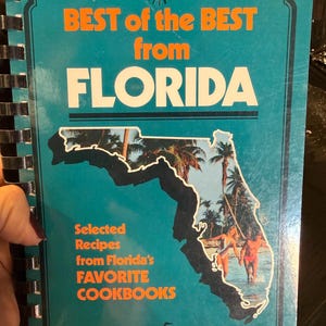 May include: A teal cookbook titled "BEST of the BEST from FLORIDA" with orange and white text. The cover features a Florida map outline with a beach scene. The book is spiral-bound.
