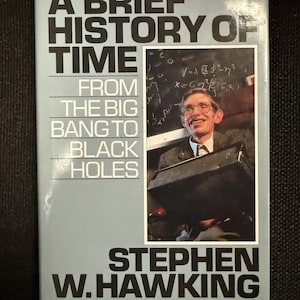 May include: A book titled "A Brief History of Time" by Stephen W. Hawking. The cover is light blue with black text and a photo of the author. The book's subtitle is "From the Big Bang to Black Holes."