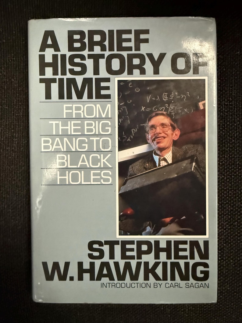 May include: A book titled "A Brief History of Time" by Stephen W. Hawking. The cover is light blue with black text and a photo of the author. The book's subtitle is "From the Big Bang to Black Holes."