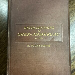 Puede incluir: Un libro marrón con letras doradas en la portada. El título es "Recollections of Ober-Ammergau in 1871" de H.N. Oxenham.