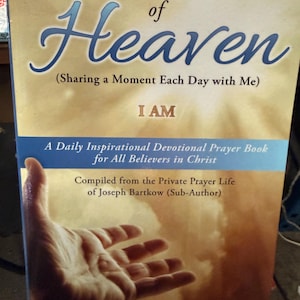 May include: A book titled Living on The Edge of Heaven (Sharing a Moment Each Day with Me) I AM. The cover features a light blue band, text stating A Daily Inspirational Devotional Prayer Book for All Believers in Christ, and a hand.
