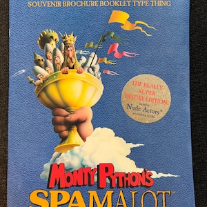 May include: A blue souvenir brochure for Monty Python's Spamalot. The cover features a golden chalice held by a hand, with cartoon characters and the text "Monty Python's Spamalot". Additional text includes "The Award-Seeking Lavishly Hand-Tooled Souvenir Brochure Booklet Type Thing."