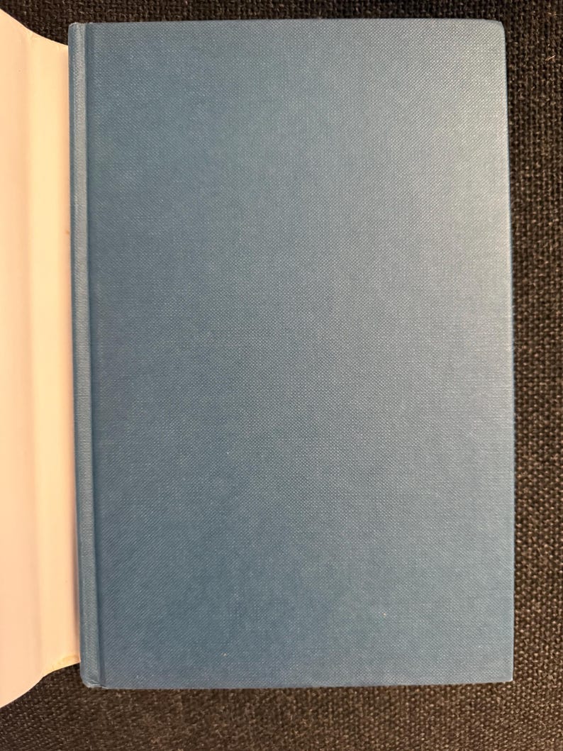 May include: A hardcover book with a light blue cover. The book is open, revealing the white pages on the left side. The cover has a textured appearance.