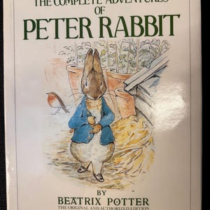 Puede incluir: Portada de "Las Aventuras Completas de Peter Rabbit" de Beatrix Potter. Ilustración de acuarela de Peter Rabbit con chaqueta azul, un pájaro y un jardín. Edición original y autorizada, nuevas reproducciones en color.
