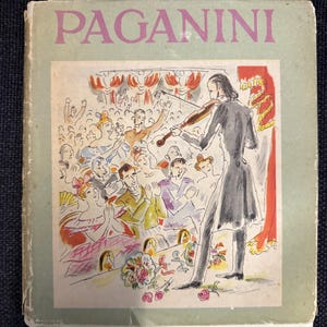Könnte beinhalten: Ein Vintage-Buchcover mit dem Titel "PAGANINI" in rosa Buchstaben. Die Illustration zeigt einen Geiger auf der Bühne, der vor einem Publikum spielt. Das Kunstwerk ist farbenfroh und stilisiert, mit Fokus auf die Aufführung und die Reaktion des Publikums.
