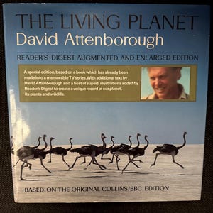 May include: A book cover for "The Living Planet" by David Attenborough. The cover features a blue background with the title in white and a photo of running ostriches. Text includes "Reader's Digest Augmented and Enlarged Edition."
