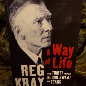 May include: A black and white book cover with a photo of a man in a suit and tie. The title of the book is "A Way of Life" and the author is "Reg Kray". The subtitle is "Over Thirty Years of Blood, Sweat and Tears".