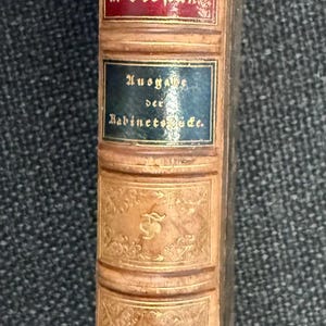 May include: A white ceramic mug with a black handle and the text "But First, Coffee" in a handwritten style. The mug is on a white surface. The mug is approximately 4 inches tall.