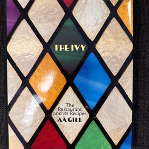 May include: A book titled "THE IVY" with a stained-glass design cover. The cover has a diamond pattern in gold, blue, red, green, and purple. The text "The Restaurant and its Recipes AA GILL" is also visible on the cover.