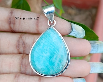 May include: A teardrop-shaped pendant with a light blue green gemstone set in a silver frame. The pendant is held in a hand.