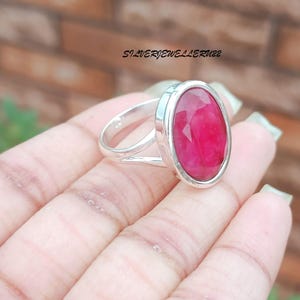 May include: A silver ring featuring a large oval ruby gemstone. The ring has a simple, elegant design.