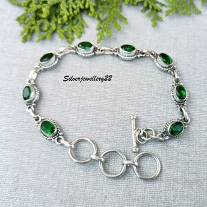 May include: A silver bracelet with a toggle clasp and green oval-shaped gemstones. The bracelet is on a gray background.