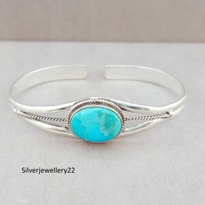May include: A silver cuff bracelet featuring a central oval turquoise stone with a smooth finish. The band is constructed from two polished silver wires that split to frame the stone, accented by a twisted rope detail. Text reads Silverjewellery22.