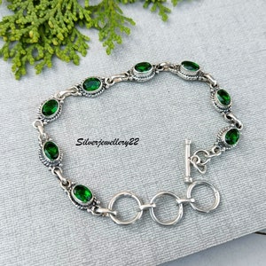 May include: A silver bracelet with a toggle clasp and green oval-shaped gemstones. The bracelet is made of sterling silver and features a delicate design.