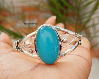 May include: A silver bangle bracelet with a large, oval-shaped turquoise gemstone. The bracelet has a delicate, swirling design.