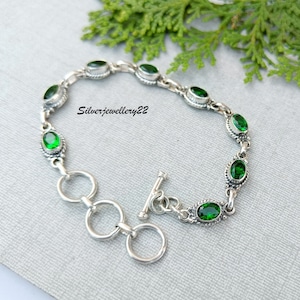 May include: A silver bracelet with a toggle clasp and green oval-shaped stones. The bracelet is made of sterling silver and features a delicate chain design.