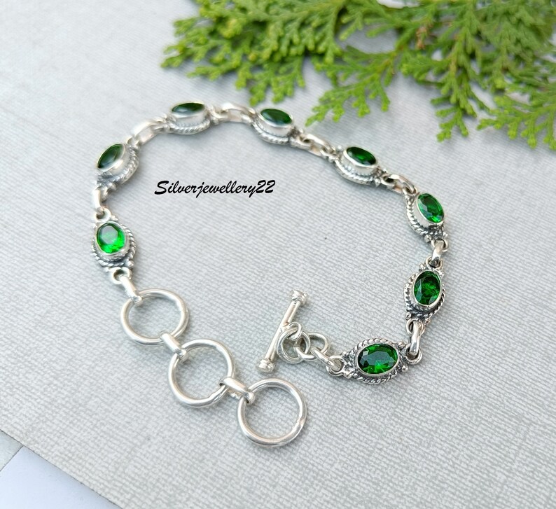 May include: A silver bracelet with a toggle clasp and green oval-shaped stones. The bracelet is made of sterling silver and features a delicate chain design.