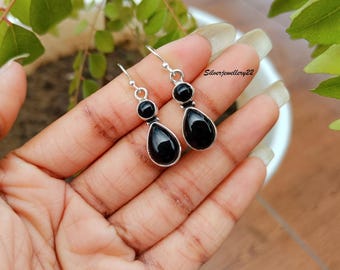 May include: A pair of silver dangle earrings with black teardrop-shaped stones. The earrings have a simple design and are perfect for everyday wear.
