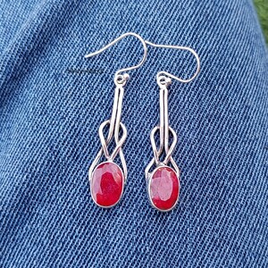 May include: A pair of silver dangle earrings with red gemstone drops. The earrings have a delicate, intricate design.
