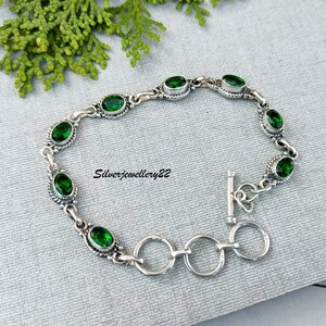 May include: A silver bracelet with a toggle clasp and green oval-shaped gemstones. The bracelet is made of sterling silver and features a delicate design.