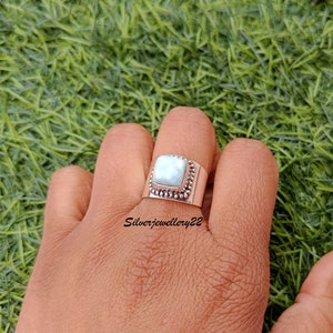 May include: A silver ring featuring a square, light blue gemstone set in a beaded bezel. The ring is worn on a hand, with the text "Silverjewellery22" visible below the ring.