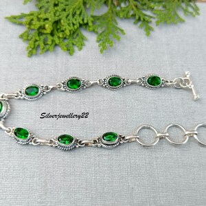 May include: A silver bracelet with a toggle clasp and green oval-shaped gemstones. The bracelet has a delicate chain design.