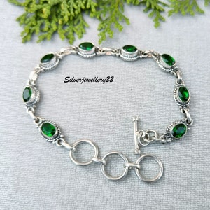 May include: A silver bracelet with a toggle clasp and green oval-shaped gemstones. The bracelet is on a gray background.