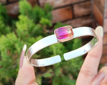 May include: A silver bangle bracelet with a large, rectangular, multi-colored gemstone set in the center.