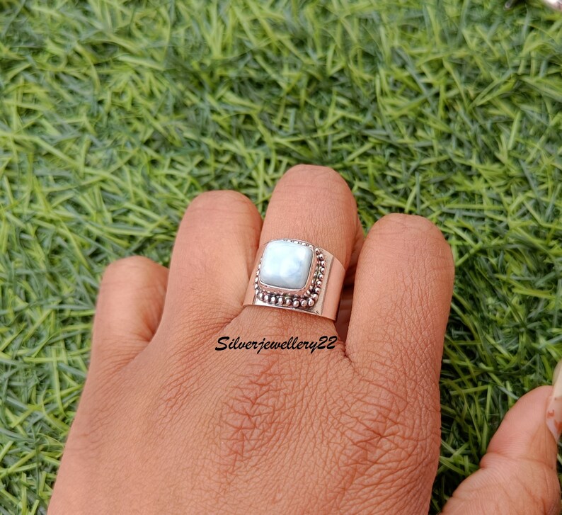 May include: A silver ring featuring a square, light blue gemstone set in a beaded bezel. The ring is worn on a hand, with the text "Silverjewellery22" visible below the ring.