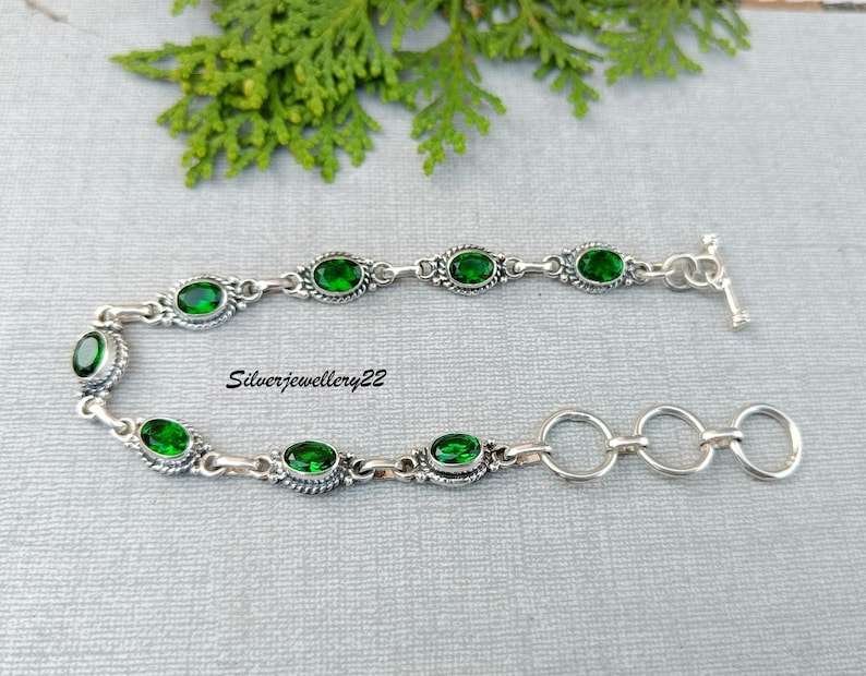 May include: A silver bracelet with a toggle clasp and green oval-shaped gemstones. The bracelet has a delicate chain design.