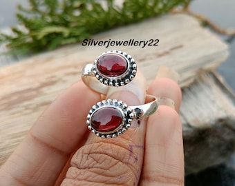 Puede incluir: Un anillo de plata con dos piedras preciosas ovaladas rojas. El anillo está diseñado para llevarse en la articulación de un dedo.