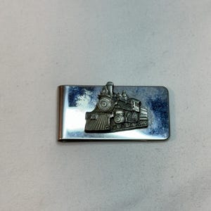 May include: A silver money clip with a detailed, three-dimensional design of a vintage steam locomotive.