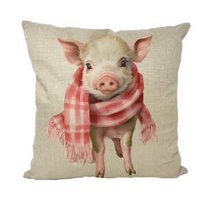 Puede incluir: Una almohada beige con una linda ilustración de un cerdo rosa con una bufanda roja y blanca a cuadros.