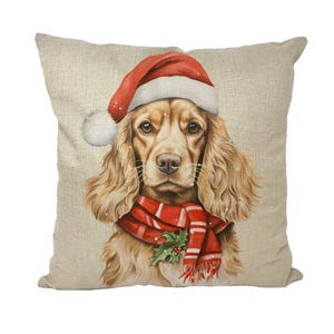 Può includere: Un cuscino quadrato decorativo con un'illustrazione ad acquerello di un Cocker Spaniel con un cappello da Babbo Natale e una sciarpa rossa a righe bianche. Il cane ha lunghi capelli ondulati marrone chiaro ed è adornato con un rametto di agrifoglio.