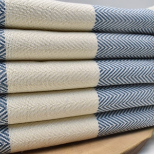 May include: A stack of blue and white striped towels with fringe edges. The towels are folded and arranged in a herringbone pattern.