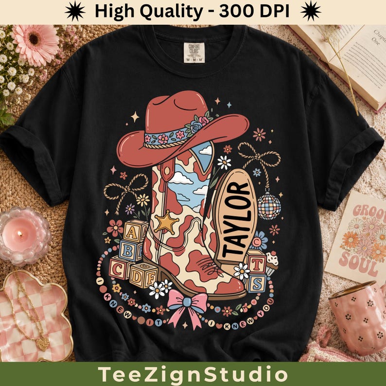 May include: A black t-shirt featuring a graphic print of a red cowboy hat and a cow-print cowboy boot. The boot displays the name TAYLOR. The design includes alphabet blocks, flowers, a disco ball, and a pink bow, with the text I KNEW IT I KNEW YOU.