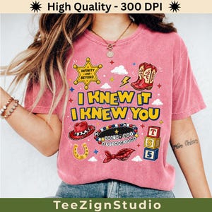 Puede incluir: Una camiseta rosa de manga corta con un estampado gr&aacute;fico que incluye una estrella de sheriff amarilla, botas de vaquero rojas, un sombrero rojo, una herradura, una pulsera de cuentas y bloques coloridos. El texto dice I KNEW IT I KNEW YOU.
