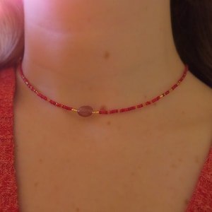 Könnte beinhalten: Eine rote und goldene Perlenkette mit einem violetten ovalen Anhänger.