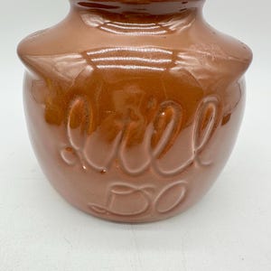 Op de afbeelding: Een bruine keramische melkkan met het woord "Melk" erop gegraveerd. De kan heeft een ronde vorm en een gladde, glanzende afwerking.