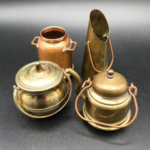 Peut inclure: Quatre miniatures de cuisine en métal. Comprend un pot à lait en cuivre, une théière en laiton avec un couvercle, un pot en laiton avec un couvercle et une pelle à charbon en laiton. Les objets sont posés sur un fond noir.