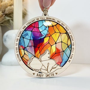 Könnte beinhalten: Ein runder Holzanhänger mit einem Buntglas-Motiv eines Babyengels. Der Anhänger ist rund und hat eine Schnur zum Aufhängen. Der Text "Second star to the right, and straight on till morning. One day this is where you will find me" ist um das Buntglas-Motiv herum geschrieben. Der Text "Baby Smith" ist unter dem Buntglas-Motiv geschrieben.