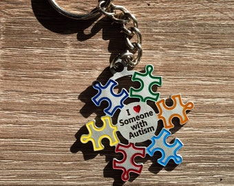 May include: A silver keychain with a colorful puzzle piece design. The puzzle pieces are arranged in a circle around a heart with the text "I love someone with Autism".