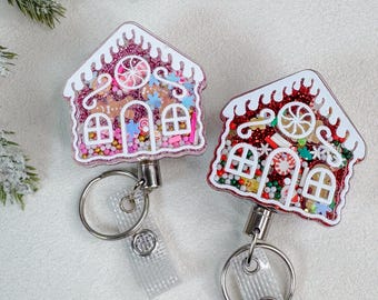 May include: Two gingerbread house badge reels featuring white outlines and clear acrylic fronts filled with colorful holiday-themed shaker confetti, including peppermint candies, snowflakes, and glitter, attached to metal key rings and clear straps.